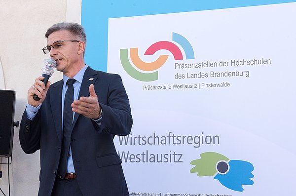 Bürgermeister der Stadt Finsterwalde Gampe während seiner Rede bei der Eröffnungsveranstaltung der Präsenzstelle Westlausitz Finsterwalde vor dem Aufsteller der Präsenzstelle und der Wirtschaftsregion Westlausitz.