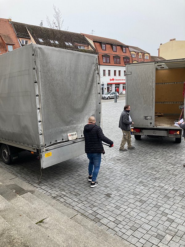 Zwei LKW von hinten aufgenommen, die zum Umbau der Präsenzstelle die Materialien und Möbel lieferten